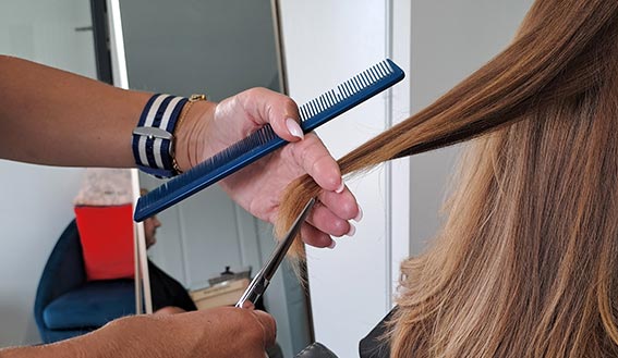 Coiffeuse qui coupe les pointes d'une mèche de cheveux d'une cliente avec un ciseau